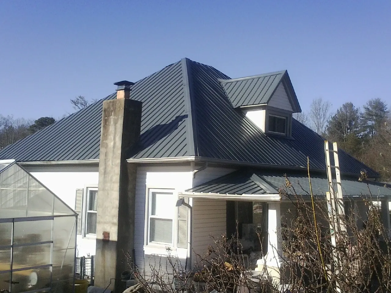 Dark blue standing seam metal roof on a white farmhouse with dormer — Slate & Tile Roof Repair by Roofing Brothers in Macomb
