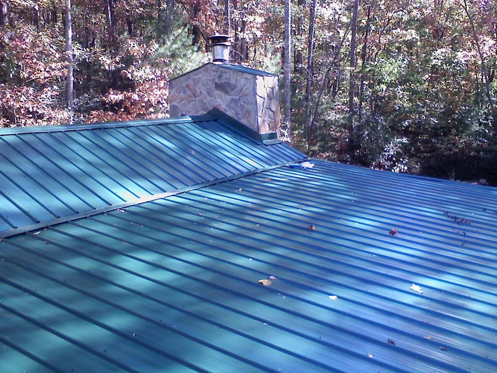 New green metal roof and stone chimney surrounded by autumn woods in Macomb