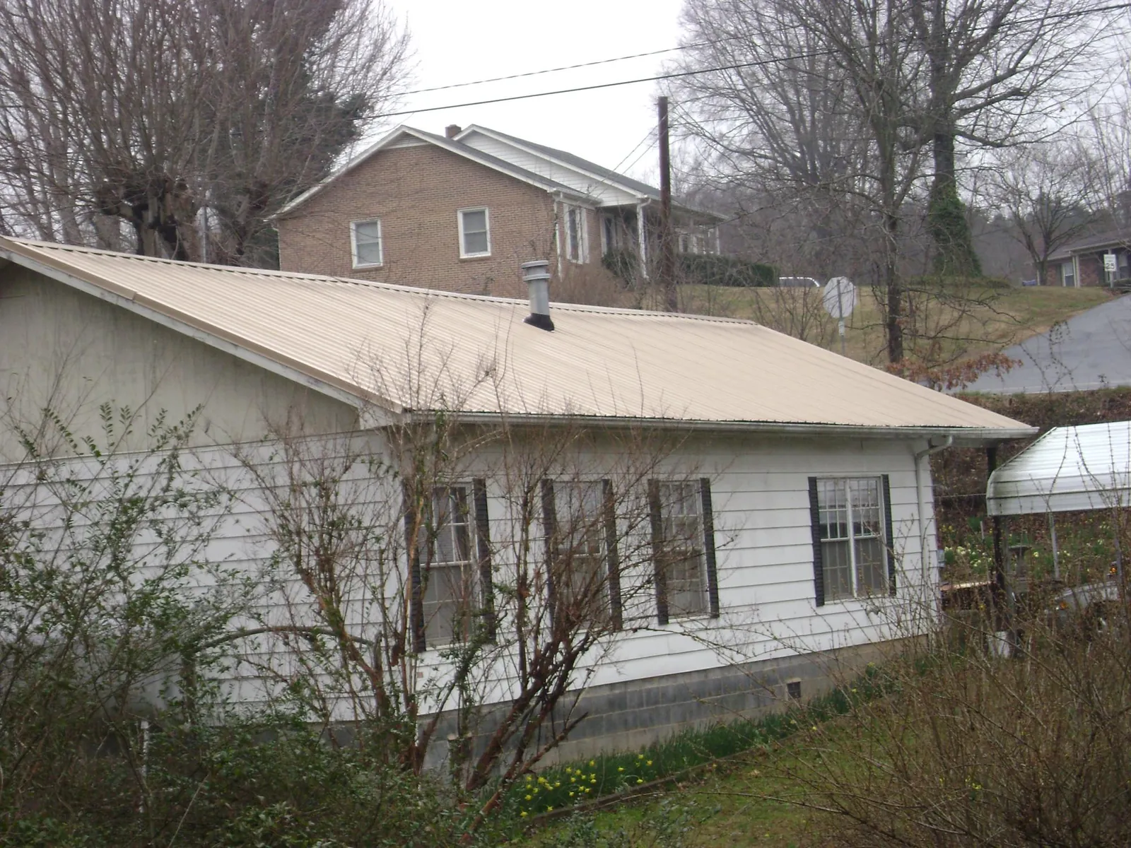 Tan metal roof on a white sided house set into a hillside — Commercial Roofing by Roofing Brothers in Macomb