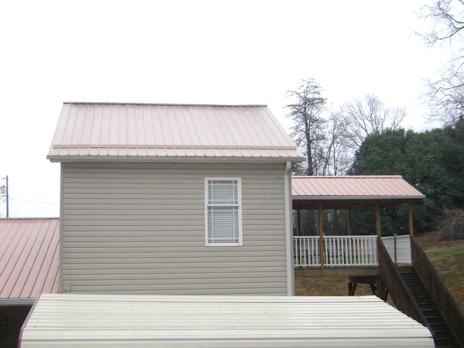 Tan metal roofs on a two story addition and attached porch, from a Roof Replacement job in Macomb